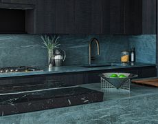 A kitchen in natural, dark stone with dark wooden cabinets and a dark marble kitchen sink