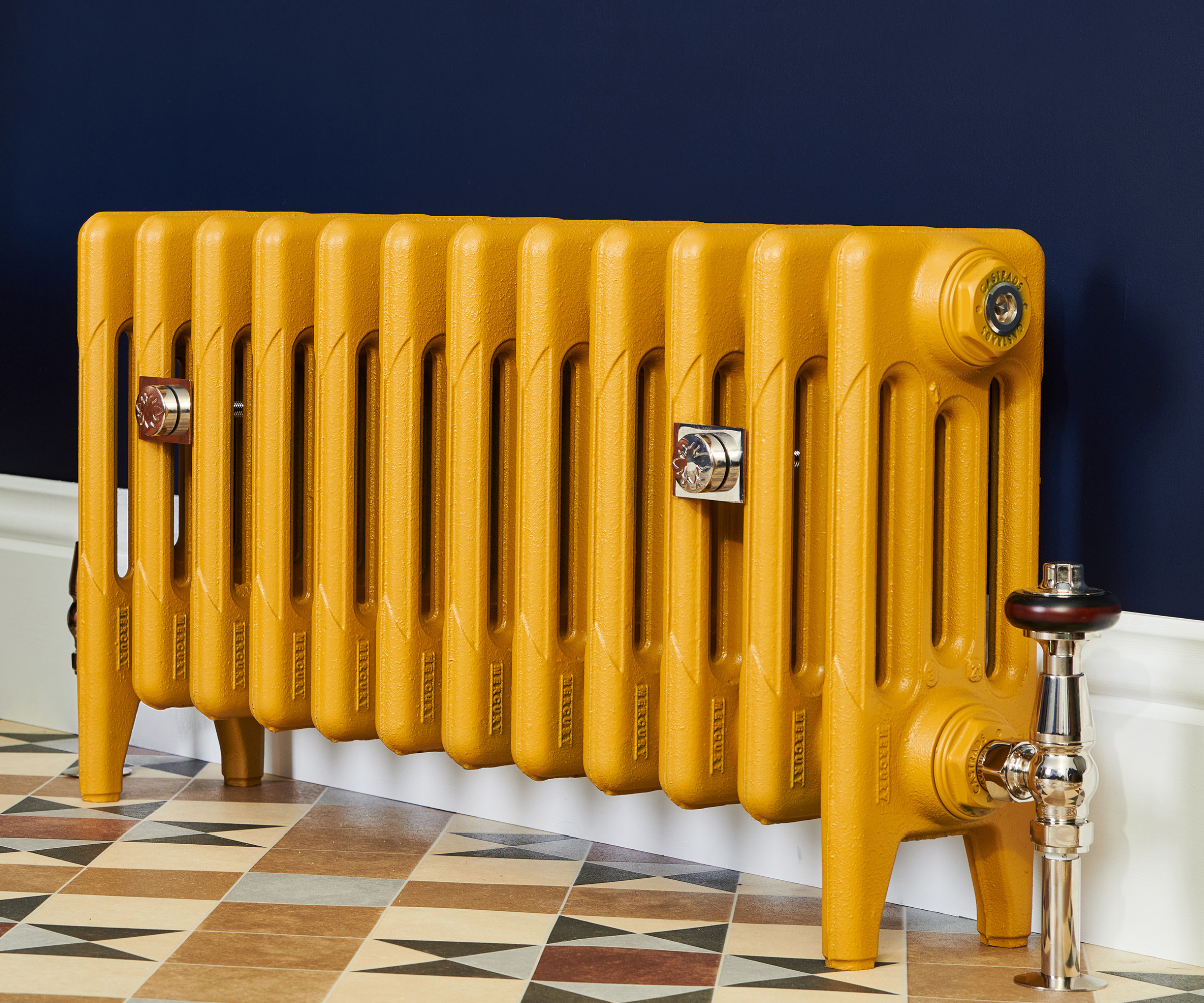 bright yellow column floor standing radiator on tiled floor with dark blue wall and white skirting board behind