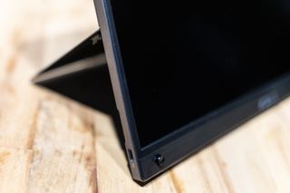 A black ASUS ZenScreen GO MB16AWP portable monitor sitting on a light wooden desk