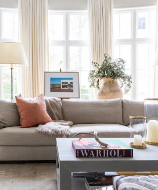 living room with cream drapes, gray couch, coffee table with books and candles, rust couch pillows, floor lamps