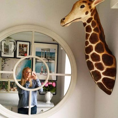 white walls mirror women with mobile phone and giraffe head statue on wall
