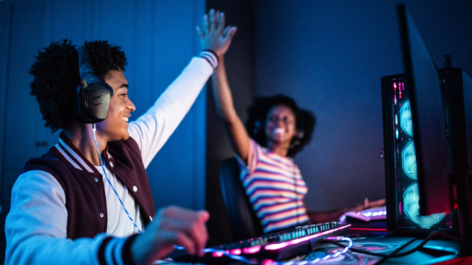 A man and woman sitting at a desk with lit-up gaming peripherals. They are high-fiving one another.