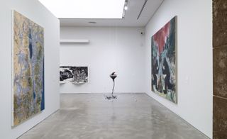 Art exhibition space with white walls. 2 large pieces of art face each other on opposing walls, and a smaller piece of artwork hangs on the end wall.