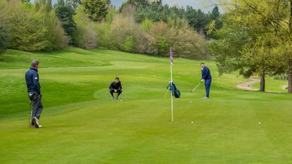 A trio of golfers watch a putt on the green