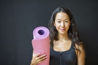 Cheerful woman holding exercise mat in fitness studio