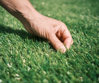 A mans hand plucking at artificial grass