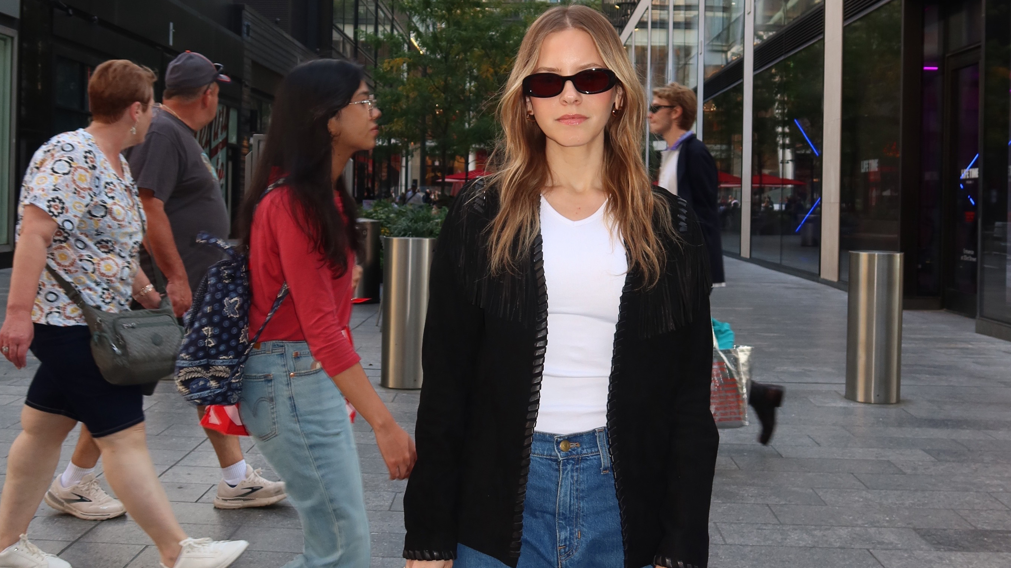 Nikki wears a white top, black jacket, and jeans.