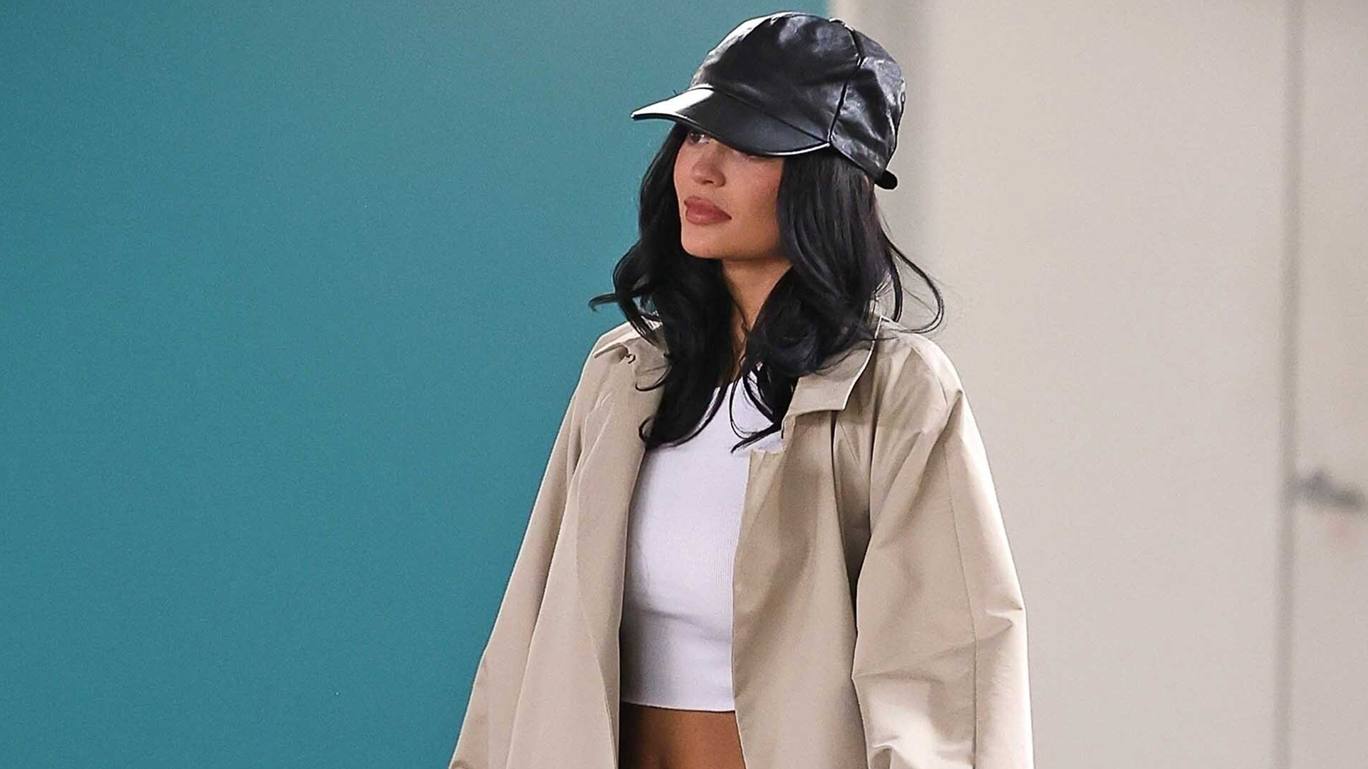 Kylie Jenner wore a trench coat with dark-wash indigo jeans, heeled flip-flops, and a leather baseball cap