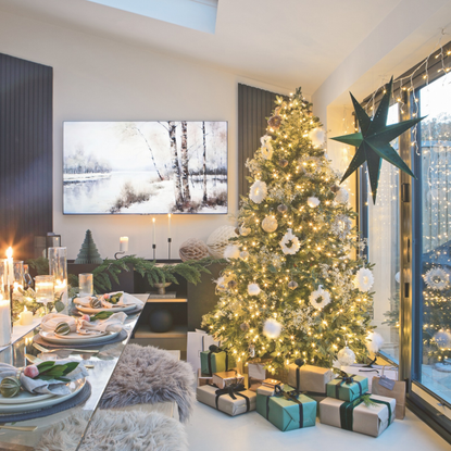 Christmas tree decorating with white ornaments and warm gold lighting next to a festive tablescape.
