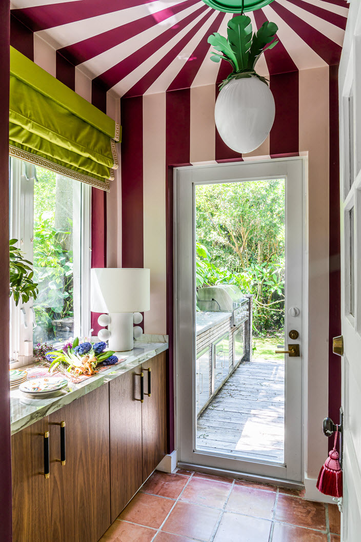 colorful laundry room with painted tented ceiling detail, hanging pendnat light, bright green roman blinds, timber cabinetry with marble counter styled with decor, and terracotta floor tiles