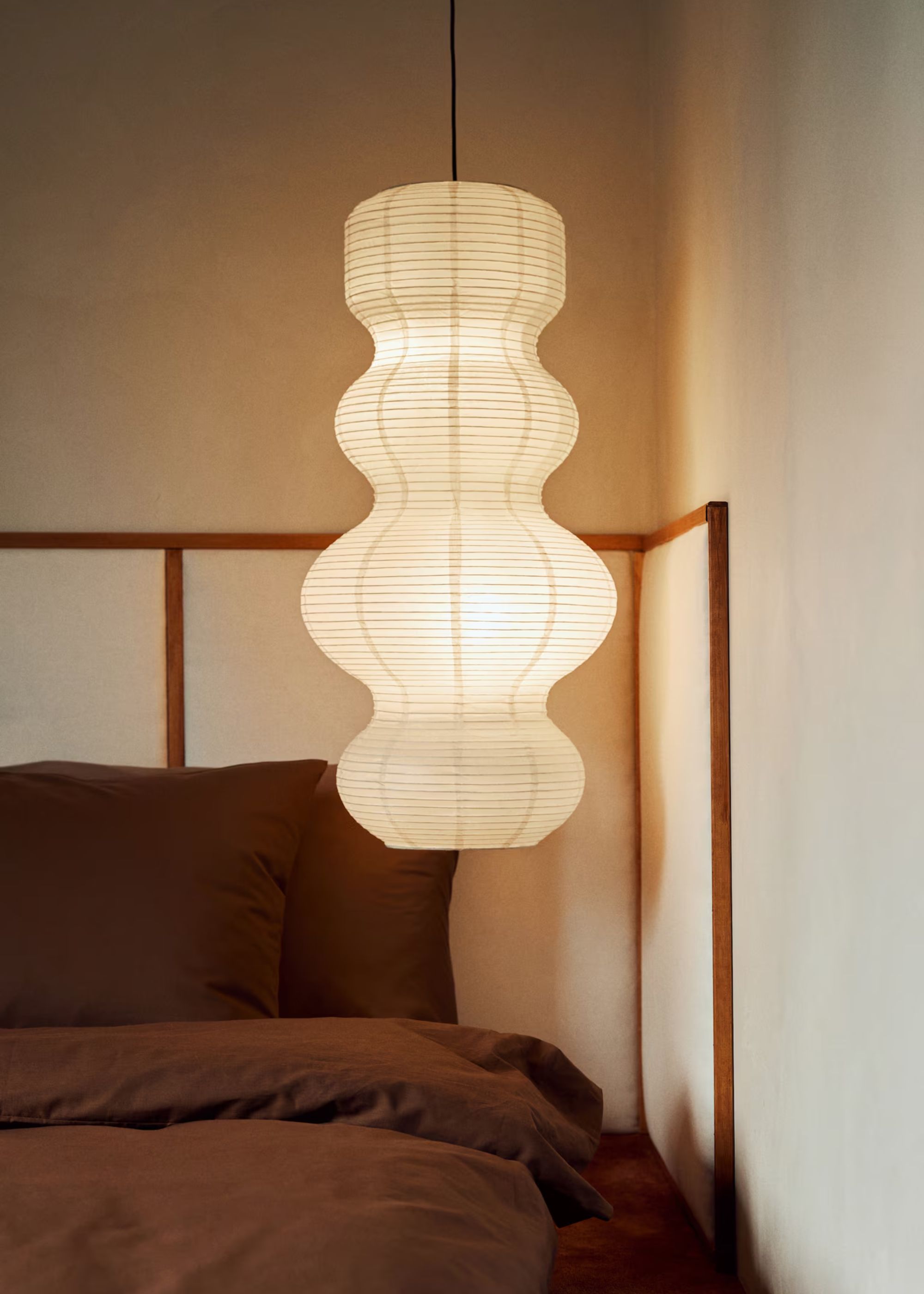 A calming bedroom with an extended headboard, a brown bedscape, and a pendant rice paper lantern