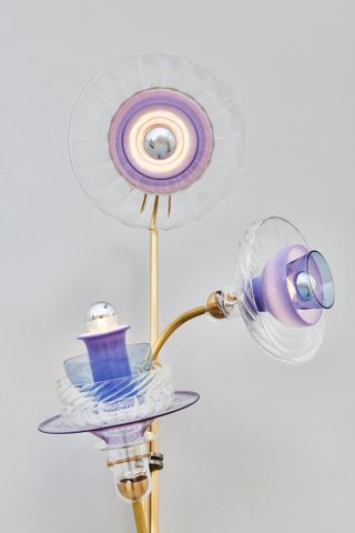 A gold triple-stemmed lamp. The lighting elements are almost flower like with a trumpet centre surrounded by glass bowls in differing shades of purple and clear glass.