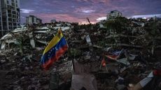 A view of the aftermath of an earthquake, with rubble everywhere and a red, yellow and blue flag in the center.