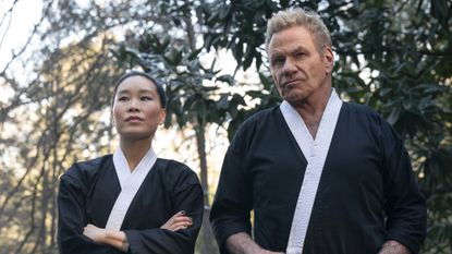 Kim and John Kreese stand in front of some trees in Cobra Kai season 6