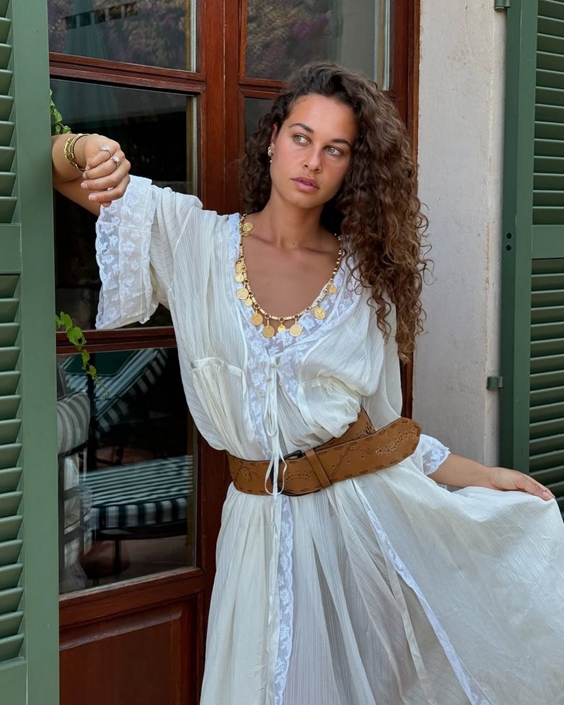 Fashion person Sarah Lysander wears a Rixo butter yellow dress, pendent necklace and brown belt. She is looking away from the camera standing in front of a brown background in a recent image take from her Instagram.
