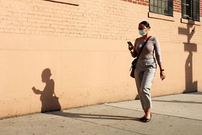 A woman wears a mask while walking down the street.