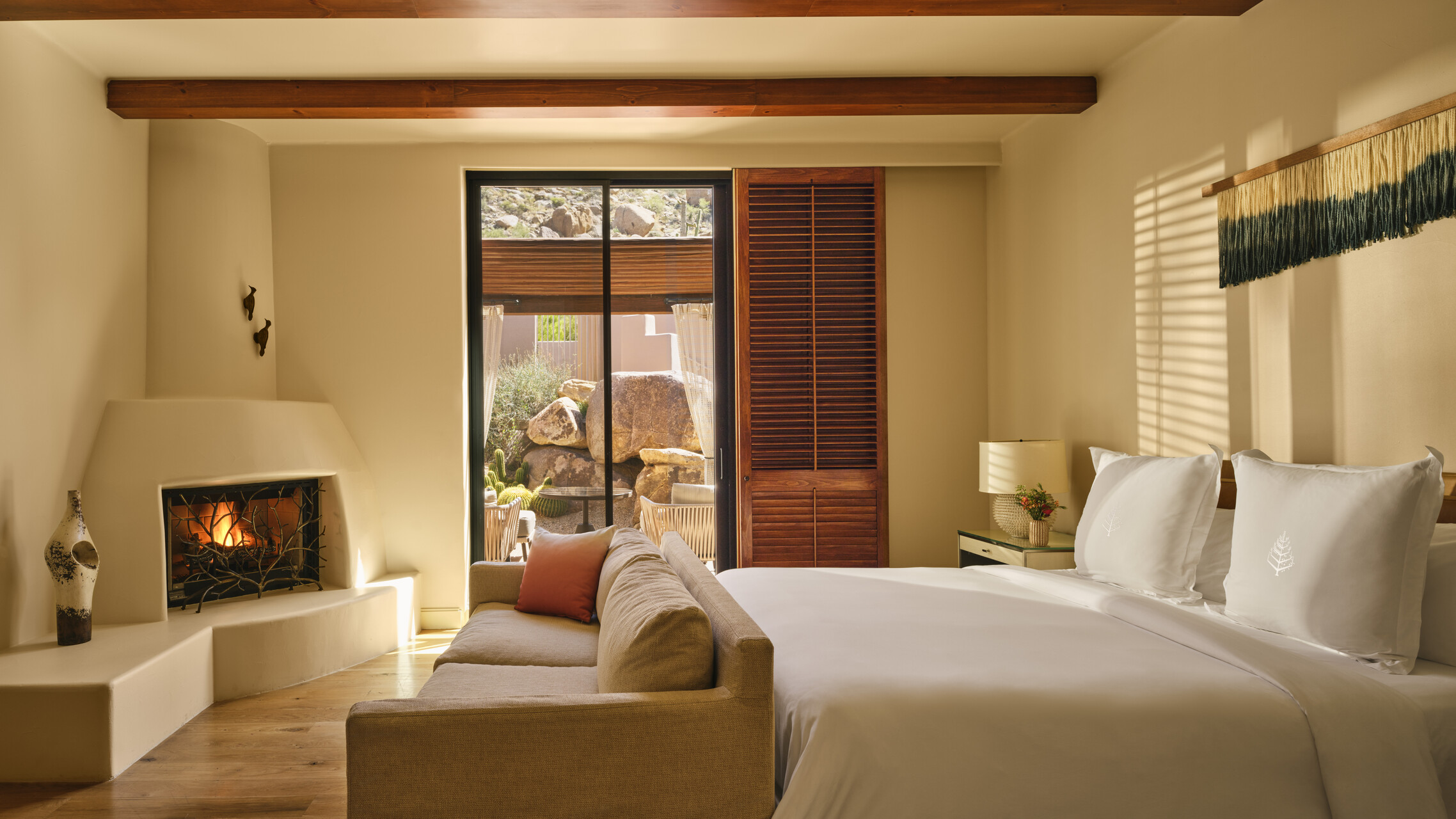 A casita-style luxury hotel suite with a lit fire, natural light coming through, and wood, beige, and terracotta furnishings.