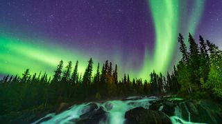 the Northern Lights put on a show over the waterfalls known as the Ramparts on the Cameron River