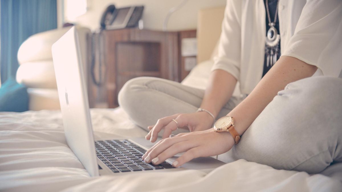 Woman typing on Apple Mac in hotel bed