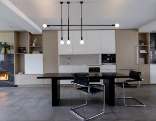 A modern minimalist kitchen with white cabinetry and black dining set, below an industrial style light fixture