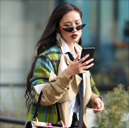 A guest wears sunglasses, a blue and green checked long wool coat, a bag with printed face-design, black leather pants, pointed high heels boots, outside Germanier, during the Womenswear Spring/Summer 2024 as part of Paris Fashion Week on September 26, 2023 in Paris, France.