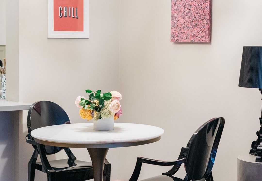 Small white-top round dining table in small apartment with black dining chairs and small bouquet plus colorful framed prints behind