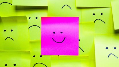 Smiley face on a pink post-it note among sad faces on yellow post-its