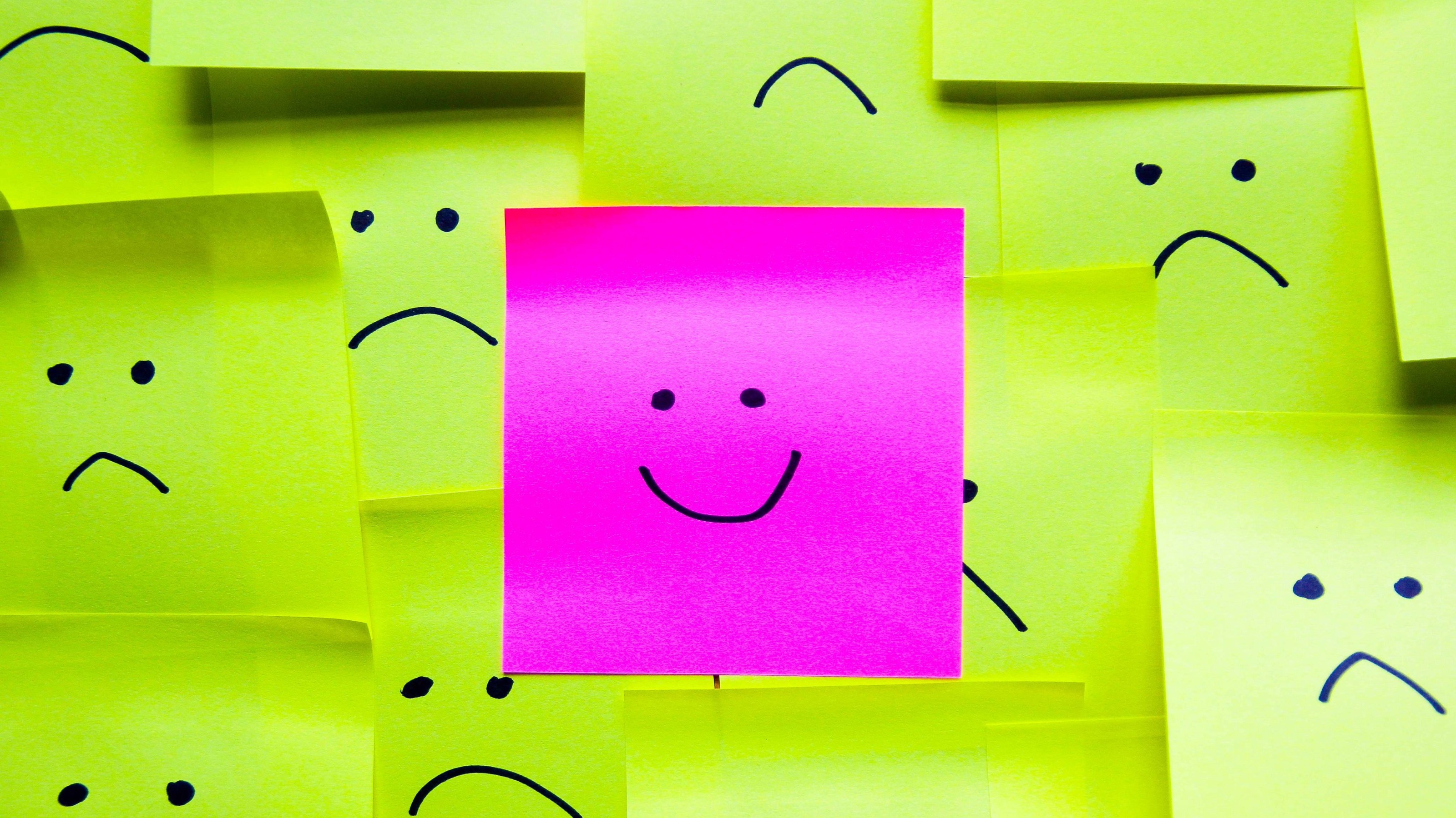 Smiley face on a pink post-it note among sad faces on yellow post-its
