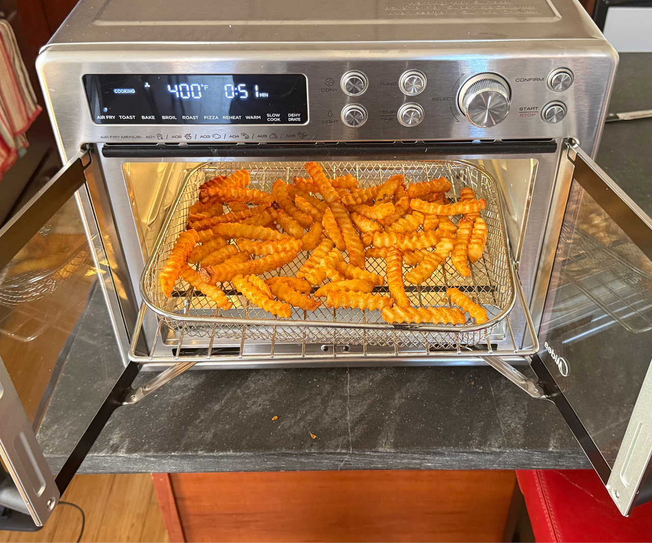 Crinkle cut fries on a wire baking tray inside a two door stainless steel air fryer oven.