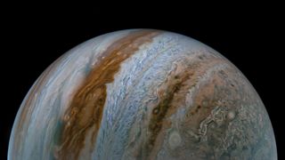 Half of Jupiter is seen rising like an orb from image bottom from the Juno spacecraft Sep. 7, with intricate stripes of different colored gasses striping the atmosphere