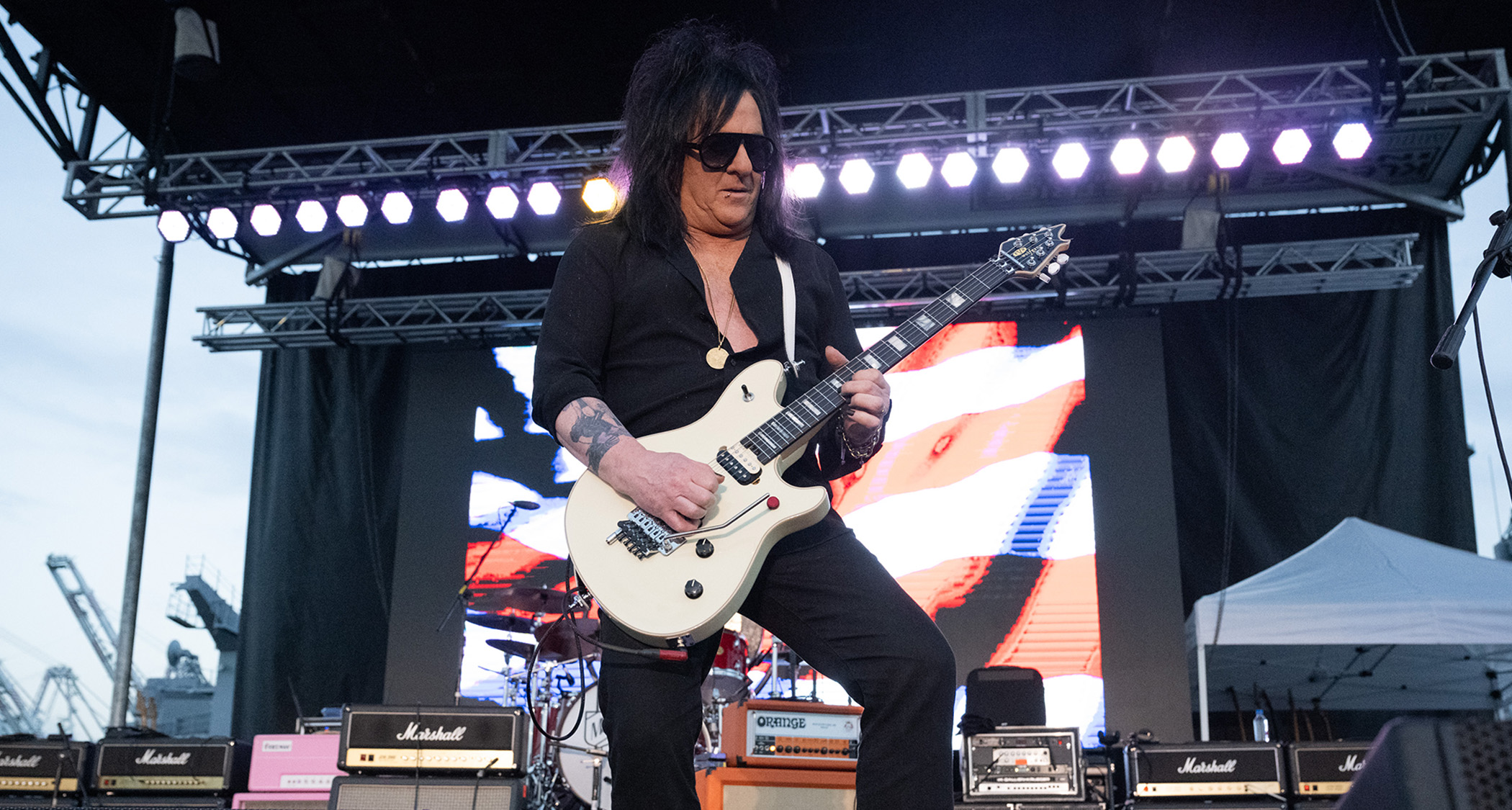 Steve Stevens shreds onstage with a red-and-white stripped video behind him.