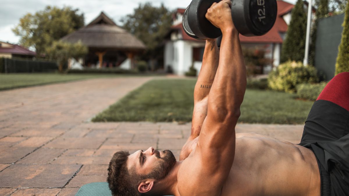 a man lying on a mat outdoors doing a dumbbell chest press