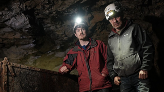 Ioan Lord and Al Tansey stand in a dark, rocky shaft wearing headlamps in Secrets of the Lost Mines