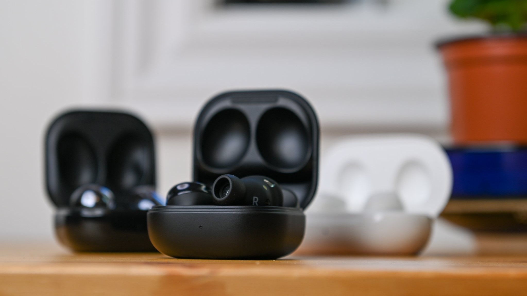 Three pairs of Samsung Galaxy Buds Pro in various colors sitting with case lids open on top of a wooden table