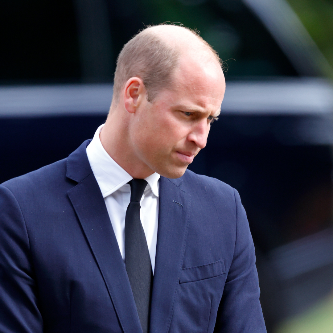 Prince William wears a navy suit and looks down at the ground, while wife Kate Middleton wears a black suit and has long brown golden hair
