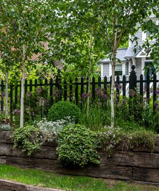 A picket fence with raised antique sleeper flower beds in front.