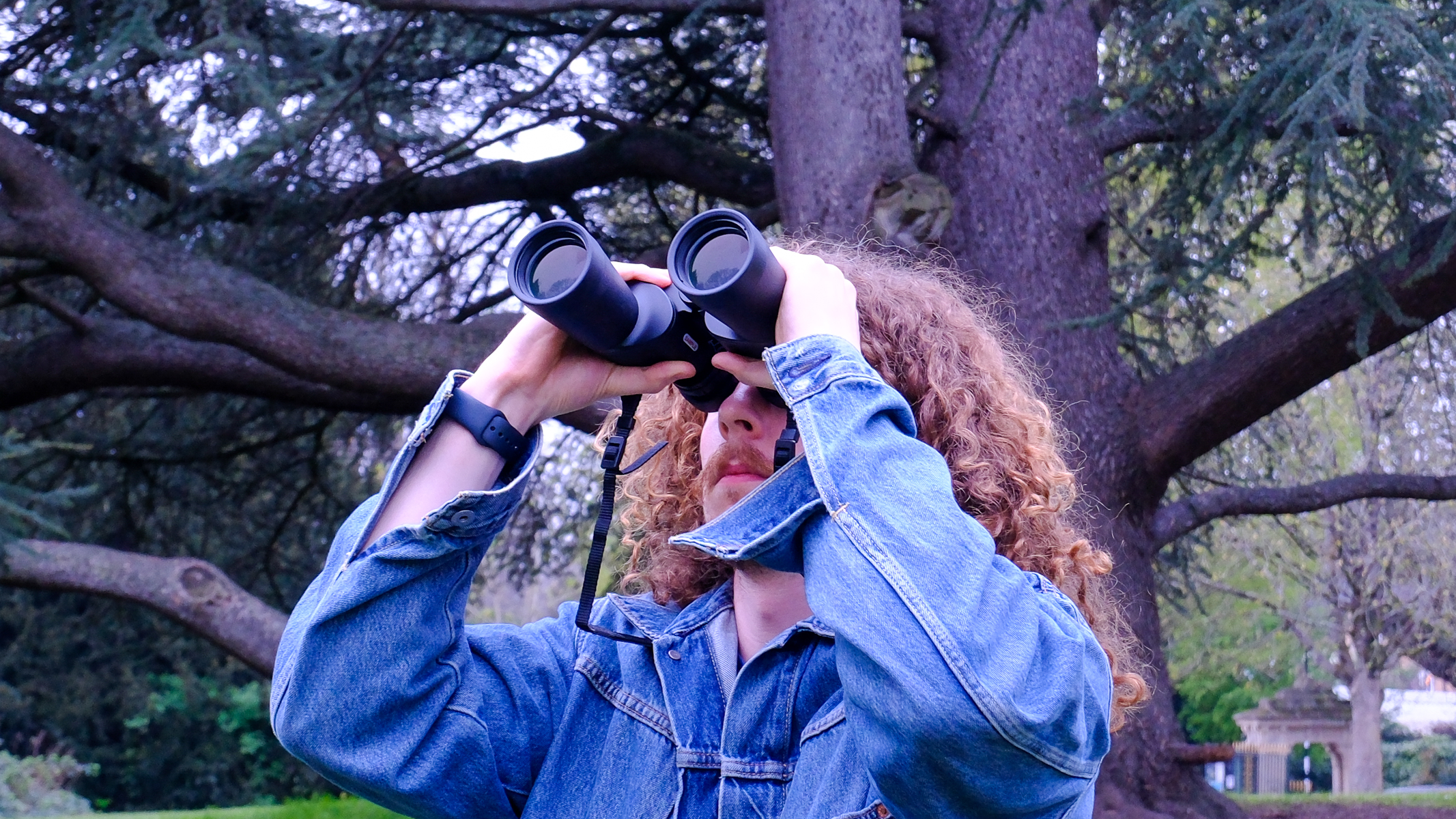 A man looking towards the sky, through the Nikon Action 7x50 binoculars, with trees in the background.