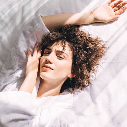 Best brightening serums - woman lying on a white sheets with face resting on her hand - getty images 1476124058