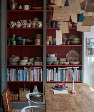 dining room with wooden table, shelving units with the backs painted dark red and lots of eclectic decor