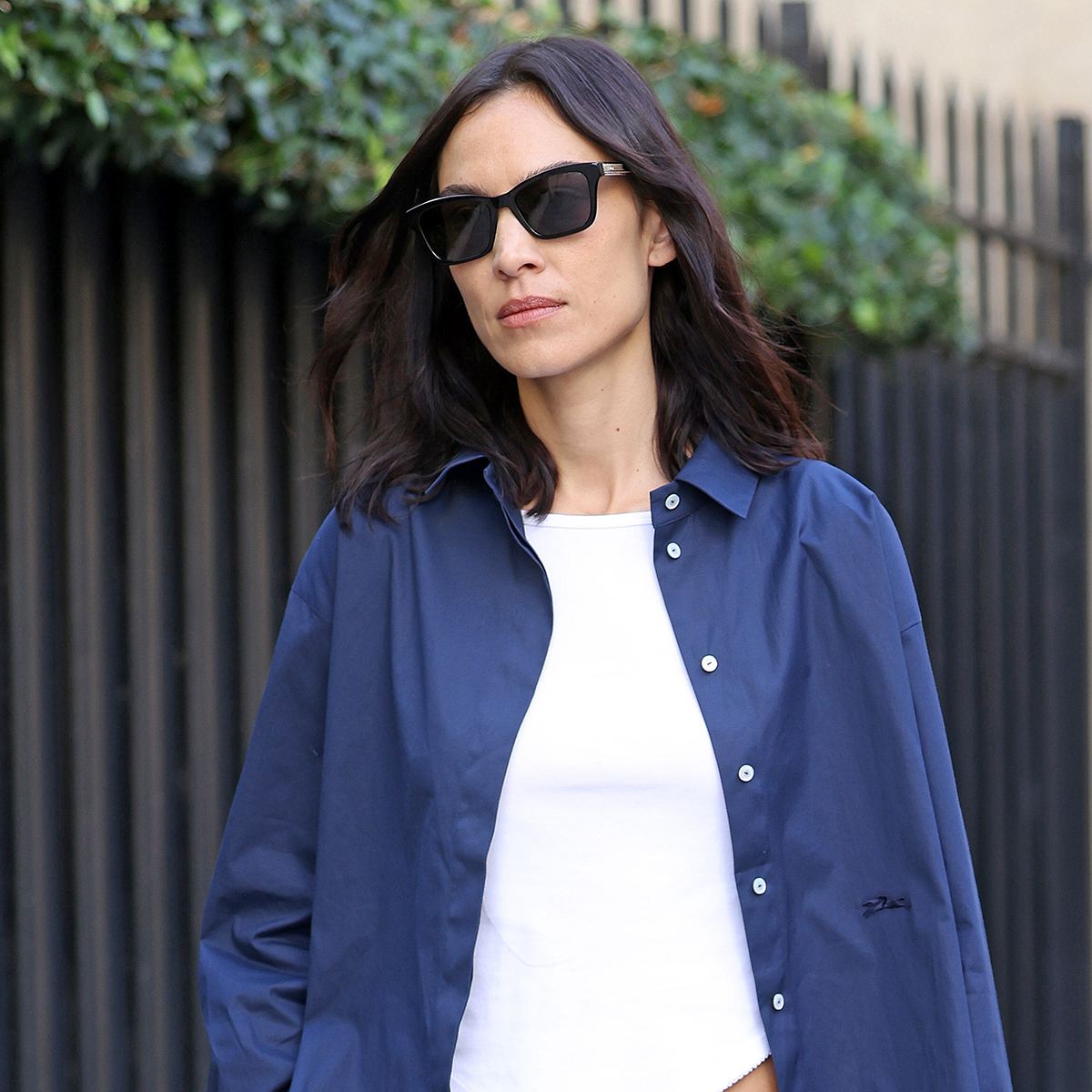 Alexa Chung wearing a blue button-down shirt over a white tee with camo pants and black ballet flats