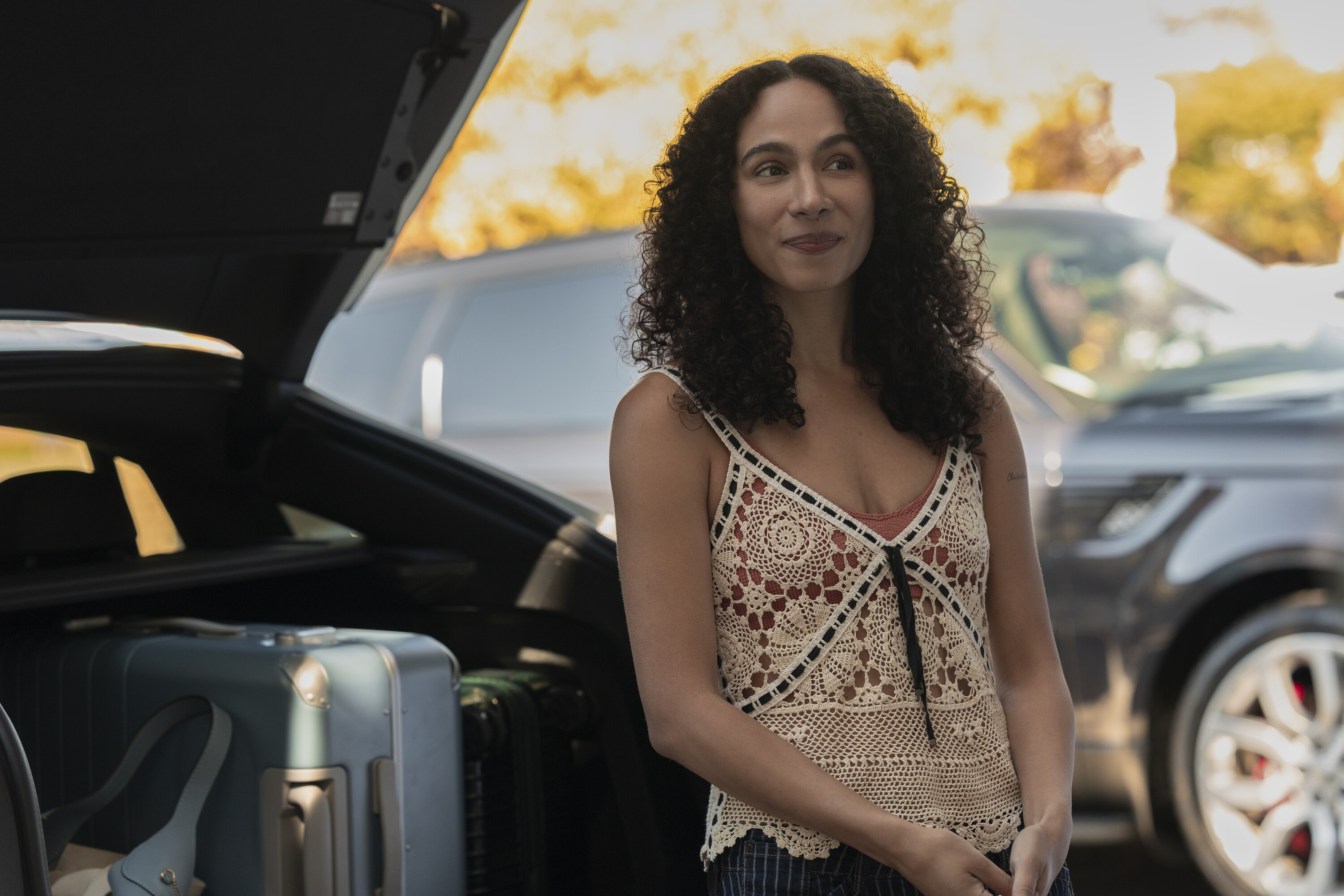 Aurora Perrineau as Chantal wearing a crocheted top and standing outside next to an open car trunk in 'Every Year After.'