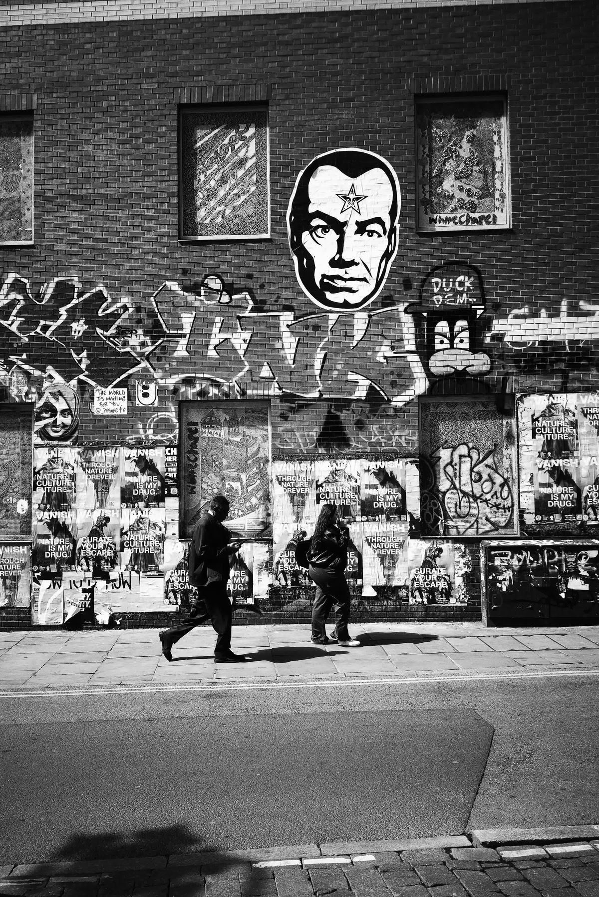 Photograph taken with the RewindPix digital compact showing street scene in high-contrast monochrome with walking figures in front of street art