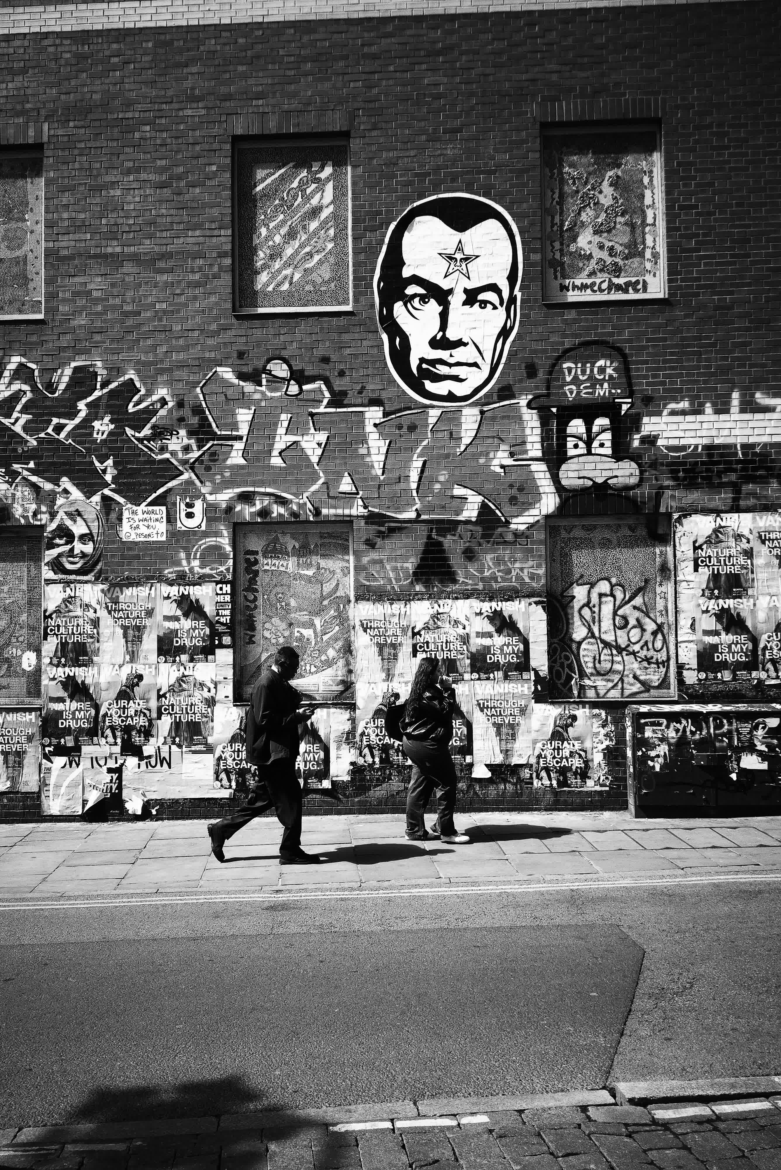 Photograph taken with the RewindPix digital compact showing street scene in high-contrast monochrome with walking figures in front of street art