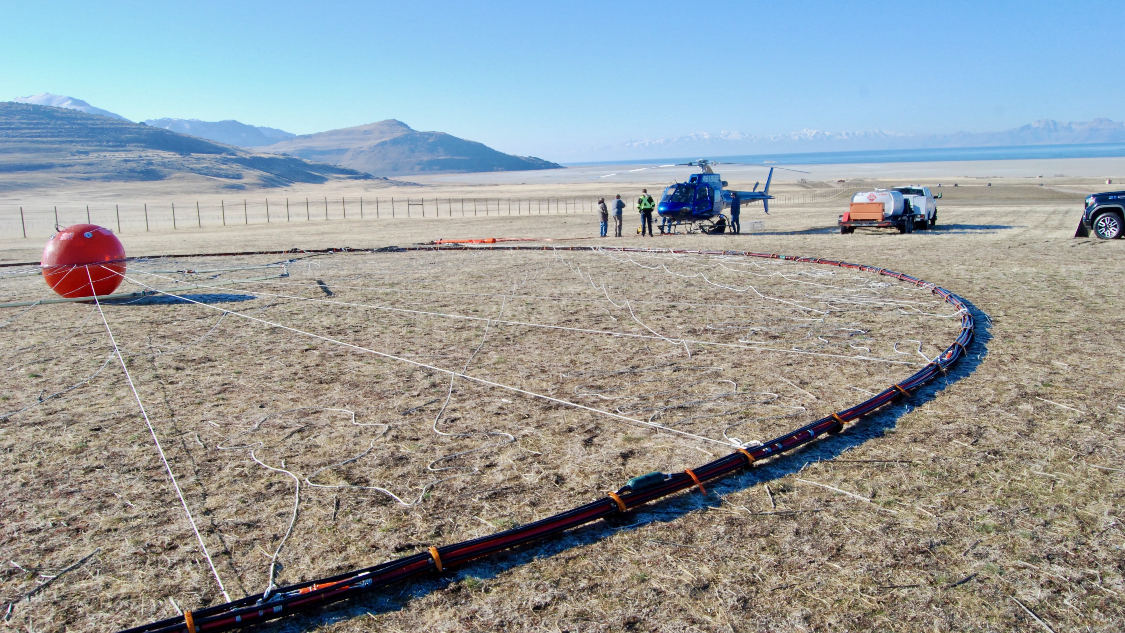 A helicopter attached to a large circular device with a ball in the center prepares for take off on Great Salt Lake.
