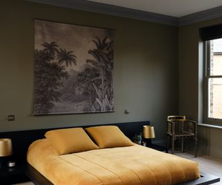 dark green bedroom with gold yellow bedding on low bed and metallic chair and lighting