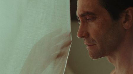 Jake Gyllenhaal looking at a hand through a curtain