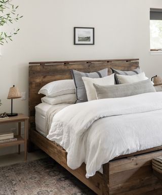 A dark wooden bed with neutral toned bedding, including grey and blue pillows