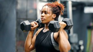Woman midway through the hammer curl and press, with dumbbells by her shoulders