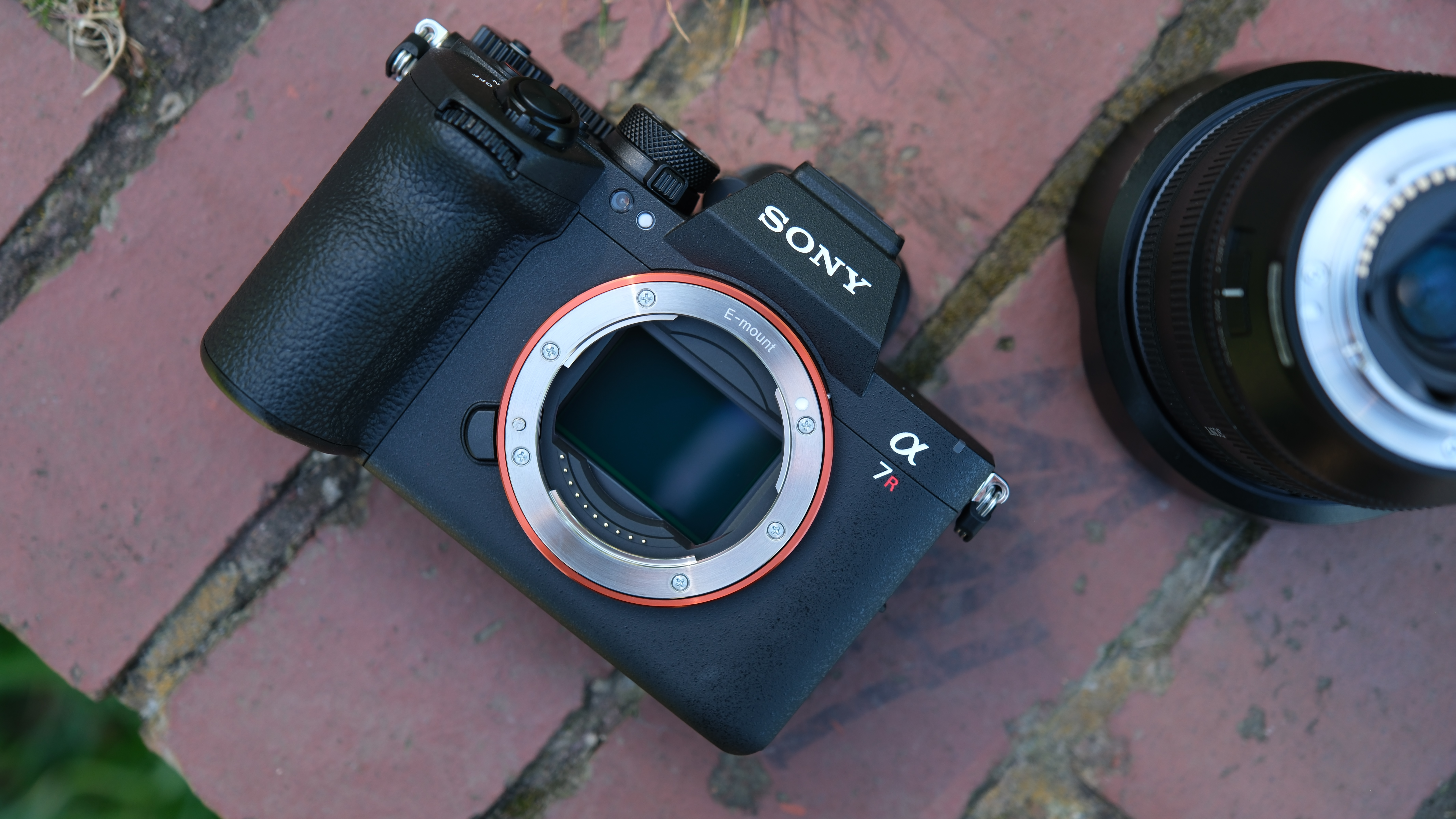 Sony A7R VI camera body with exposed E-mount sensor beside a lens on brick paving.