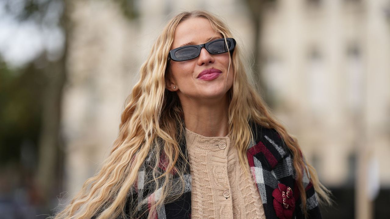 Woman with long blonde, wavy hair walks down the road during fashion week in a tartan jacke t